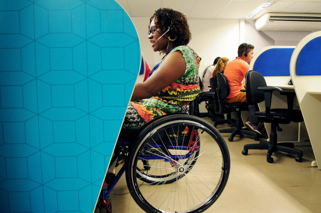 Woman using a wheelchair, wearing a headset, working at a desk in an office